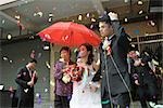Mariage chinois, la mariée et le marié laissant sous les confettis, mariée recouverte d'ombrelle rouge