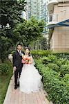 Bride and groom standing in verdant apartment complex, full length portrait