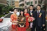 Bride and groom standing with parents and sister in front of car, portrait