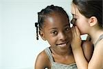 Girl smiling at camera as friend whispers in her ear