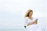 Woman listening to MP3 player, ocean horizon in background