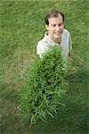 Man holding up clump of grass, smiling at camera, high angle view