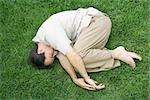 Man lying in fetal position on grass, eyes closed, high angle view