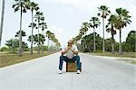 Man sitting on suitcase in the middle of street, looking away