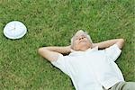 Senior homme couché sur l'herbe suivant pour l'horloge, les mains derrière la tête, grande angle vue
