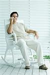 Man sitting in rocking chair, using cell phone, full length