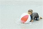 Little boy down on all fours in water, playing with beach ball