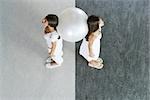 Teenage twin sisters standing back to back, supporting fitness ball between them, high angle view