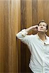 Man leaning elbow against wall, holding chin, looking up