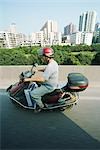 Homme de Chine, Guangzhou, monté sur moteur scooter, tours d'habitation en arrière-plan, vue latérale