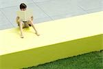 Boy sitting on low wall outdoors, reading book, high angle view