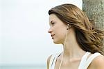 Teenage girl listening to earphones outdoors, hair tousled by breeze, looking away