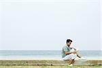 Homme assis sur la plage, en lisant le livre, vue latérale