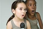 Two little girls singing into microphone together, close-up