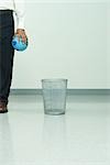 Man standing next to garbage can, holding globe in hand, cropped view