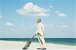 Man in suit standing on beach, using vacuum cleaner, side view