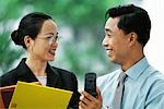 Businessman showing cell phone to female colleague, both smiling at each other