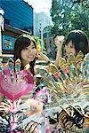 Two young women in street market, trying on hair accessories, smiling