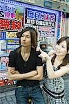 Young couple in front of Japanese storefront, looking away, woman pointing