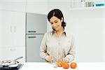 Woman standing at kitchen counter, slicing tomatoes with knife