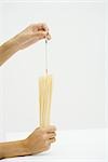 Hands holding dried pasta, measuring with stick