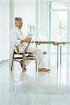 Mature man sitting at table, reading book, side view