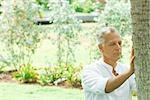 Mature man touching tree trunk, eyes closed