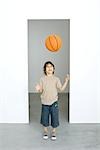 Little boy throwing basketball in the air, looking up, smiling