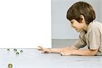 Little boy lying on the ground playing with marbles, side view