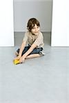 Little boy sitting on the ground, playing with toy trucks, smiling at camera