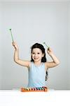 Little girl playing xylophone, arms raised, smiling