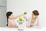 Mère et fille pesant de pommes sur échelle, souriant à l'autre, fille brandissant une pomme