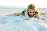 Petite fille couché dans le sable à la plage, souriant à la caméra