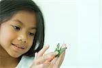 Little girl touching butterfly, looking down, smiling