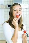 Young woman eating radish in kitchen, portrait