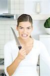 Femme tenant le couteau de cuisine, serrant les dents, en regardant la caméra, portrait