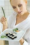 Woman holding maki sushi and chopsticks, looking down