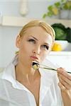 Woman holding up maki sushi with chopsticks, looking up, puckering lips