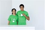 Man holding watering can, standing beside woman wearing tee-shirt printed with plant graphic, portrait