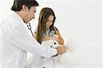 Doctor sitting with little girl, examining teddy bear with stethoscope