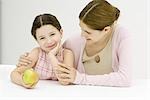 Woman and girl, girl holding apple, smiling at camera