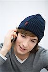 Young man in knit hat using cell phone, looking down, close-up