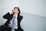 Young man in suit sitting on the ground, using cell phone, head back