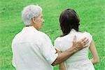 Grandfather with hand on teen granddaughter's shoulder outdoors, rear view