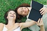 Mère et fille teen couché ensemble dans l'herbe, le rire, la femme tenant un livre