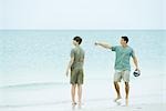Father and teen son at the beach, man holding ball and pointing, both looking away