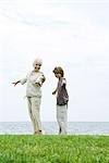 Grandmother and grandson standing outdoors with arms out, both smiling at camera, ocean in background