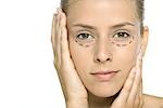 Woman with plastic surgery markings under eyes, holding face, looking at camera