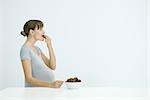 Pregnant woman eating bowl of strawberries, side view