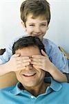 Boy with hands over his father's eyes, looking at camera, both smiling